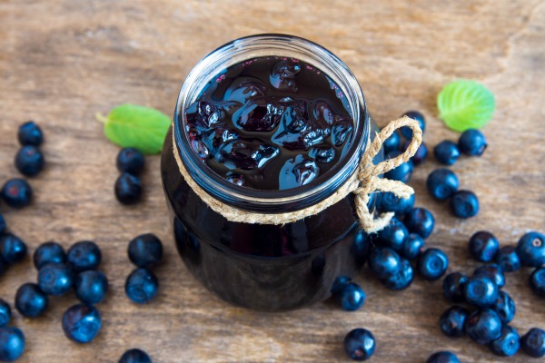 Blueberry jam in jar with berries and leaves over rustic wooden table